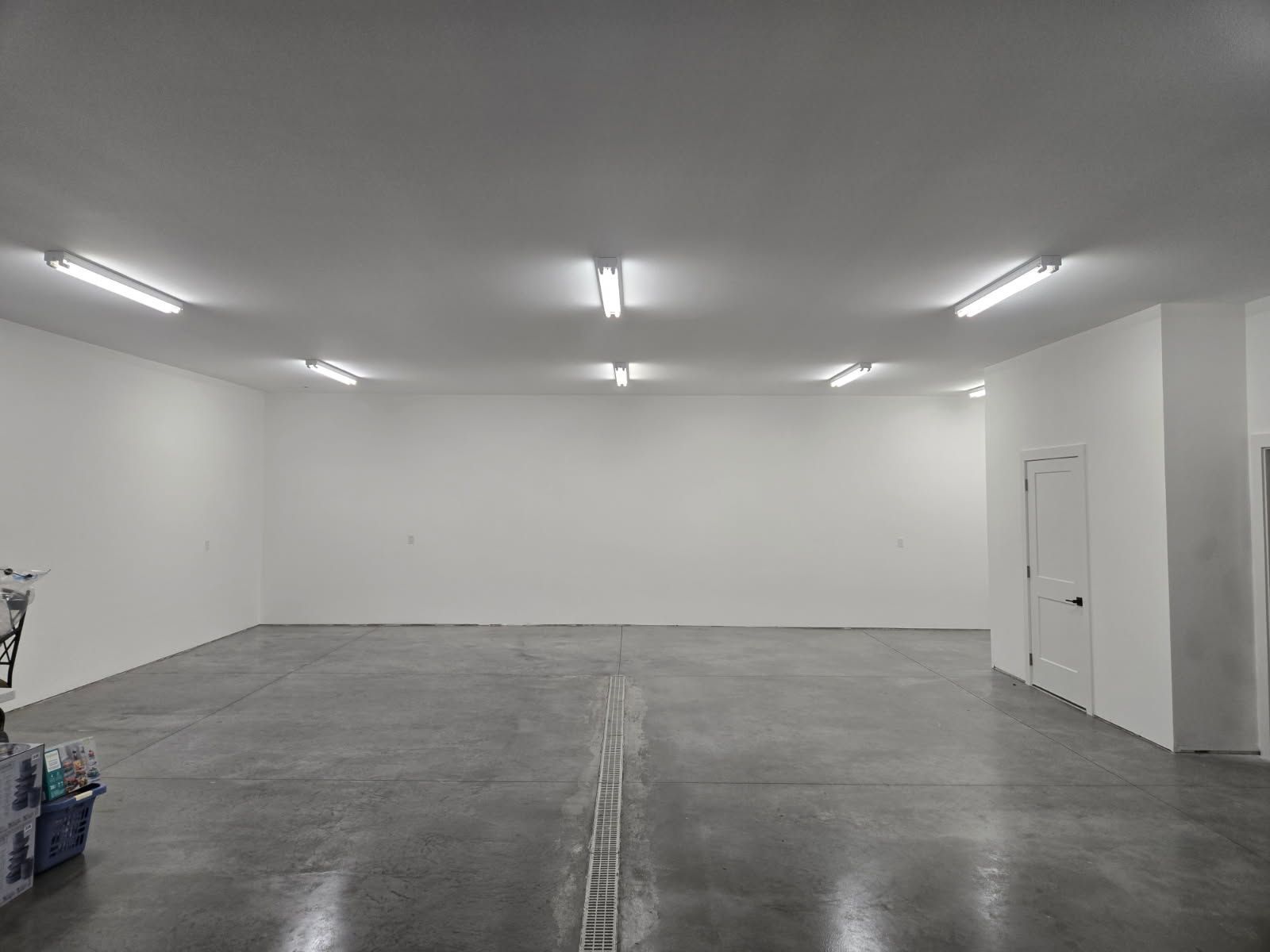 Empty white warehouse room with concrete floor and fluorescent ceiling lights