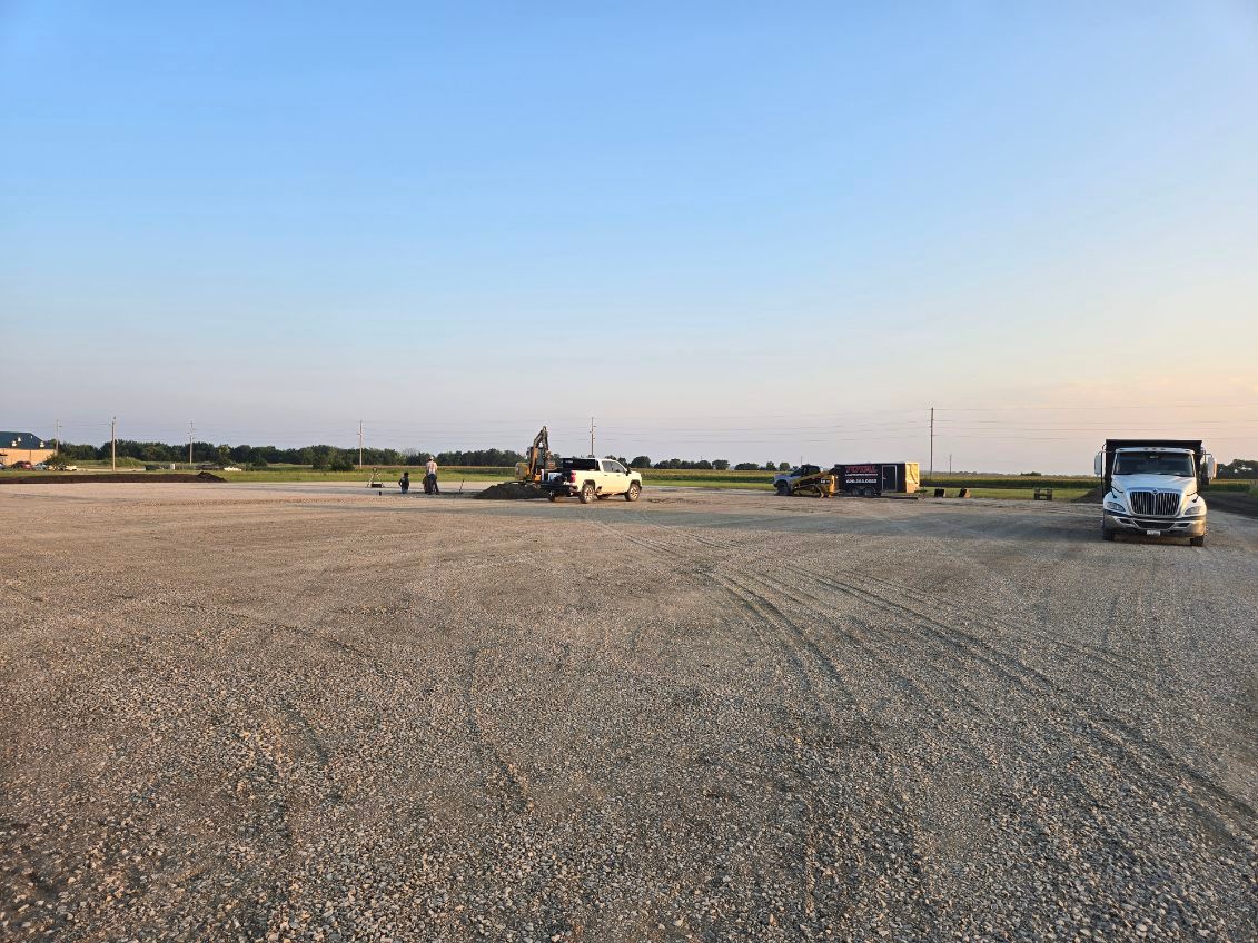 Wide gravel lot under a clear sky, with a few vehicles and equipment in the distance.