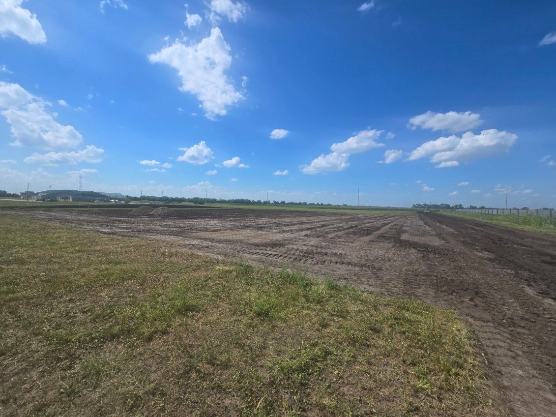 Wide open dirt field under a bright blue sky with scattered clouds.