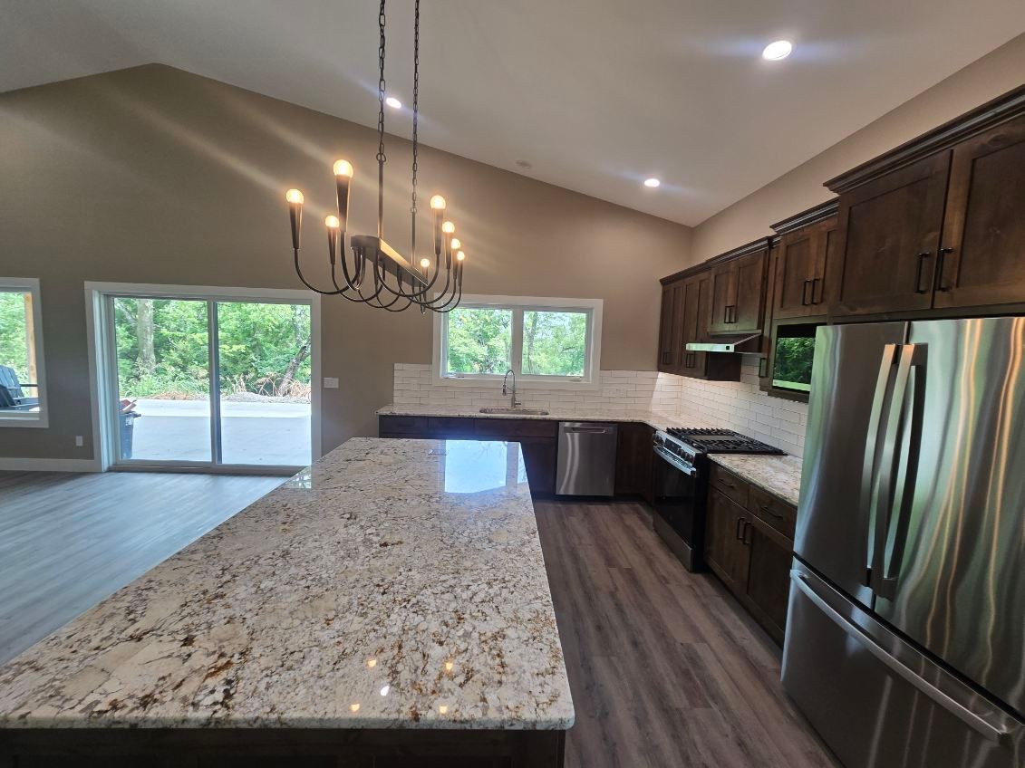 Modern kitchen with granite island, stainless steel appliances, dark wood cabinets, and chandelier near sliding glass doors