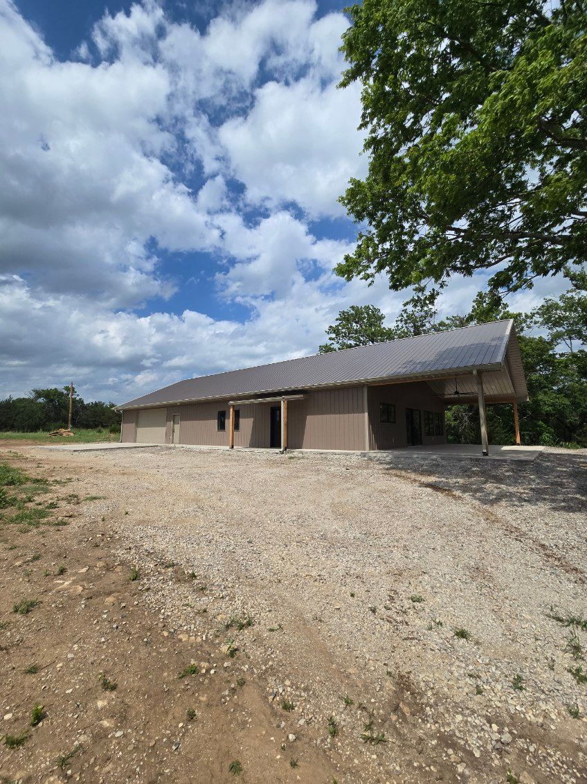 Single-story rural building with a corrugated roof on a gravel lot under a cloudy sky