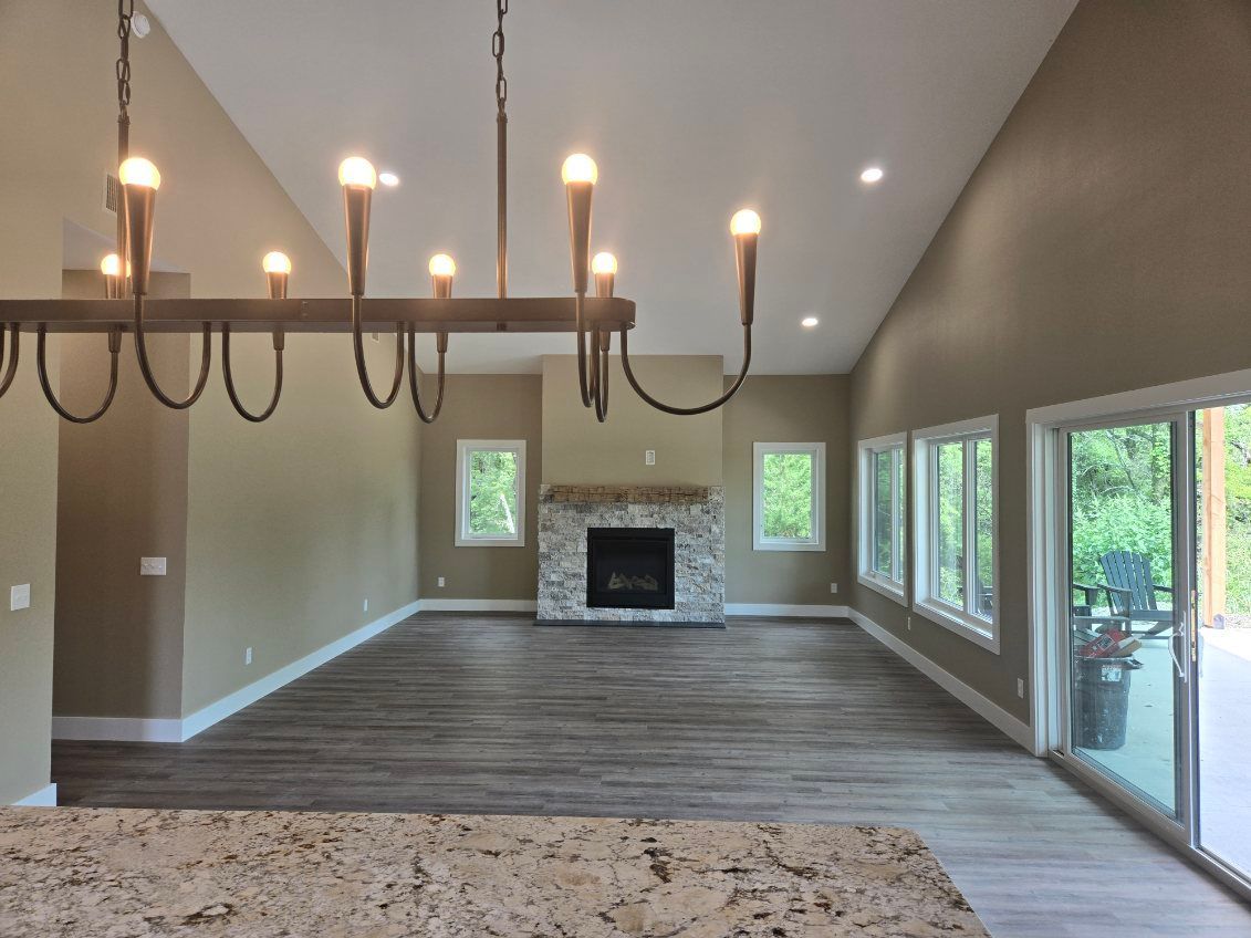 Open-concept living room with chandelier, fireplace, gray floors, and large windows overlooking greenery
