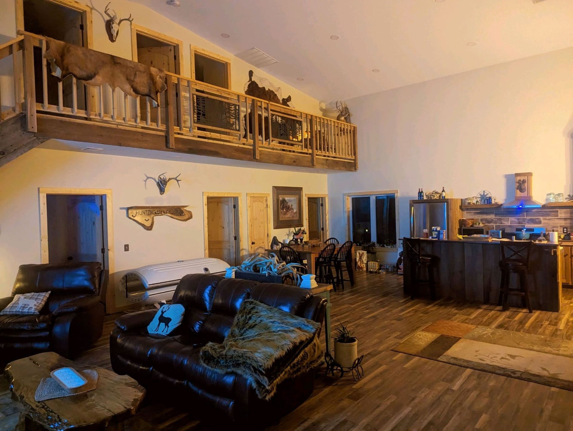 A spacious living area with a loft, wood-paneled accents, hunting decor, leather sofas, and an open-concept kitchen.