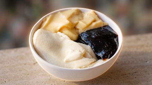 White bowl with three scoops of ice cream or mochi, including vanilla, caramel, and dark chocolate on a tabletop