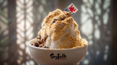Topped ice cream in a bowl with a small umbrella, against a soft blurred background.