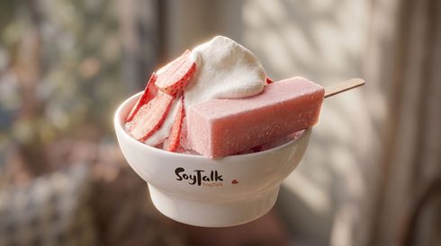 A bowl of pink shaved ice topped with cream and syrup, with a wafer stick on a spoon.