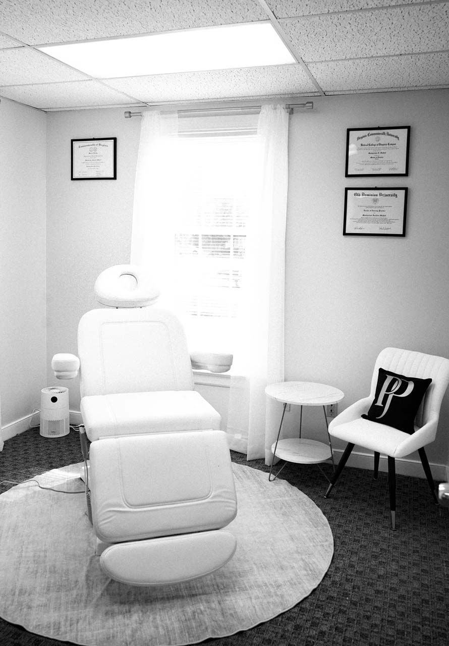 Spa treatment room with a white chair, round rug, and framed diplomas.