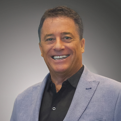Smiling man in a light gray blazer and black shirt against a neutral gray background