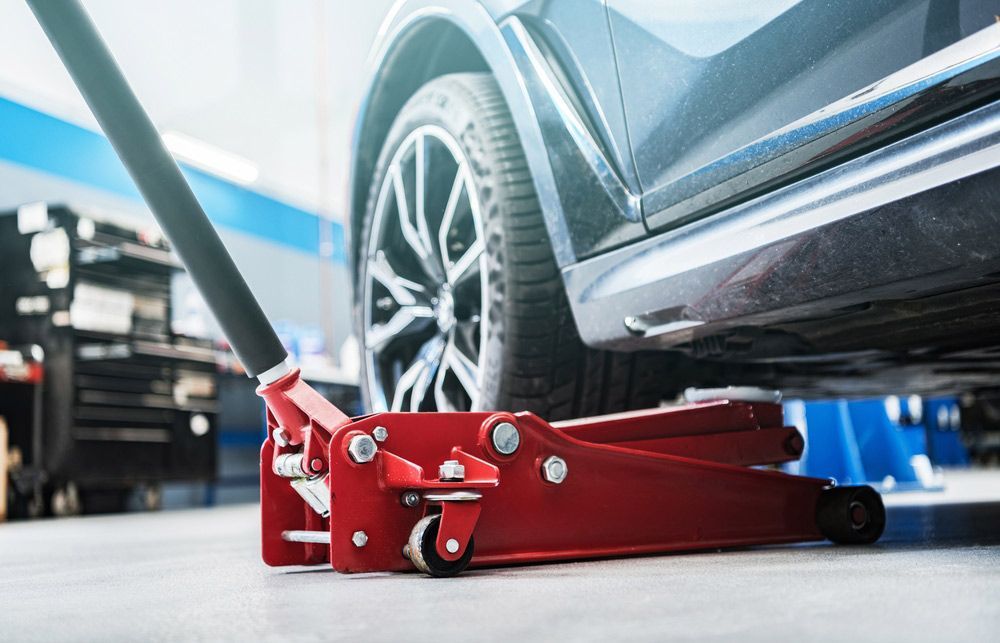 A Red Car Jack Is Sitting Under A Car In A Garage — Carson's Car Care In Armidale, NSW