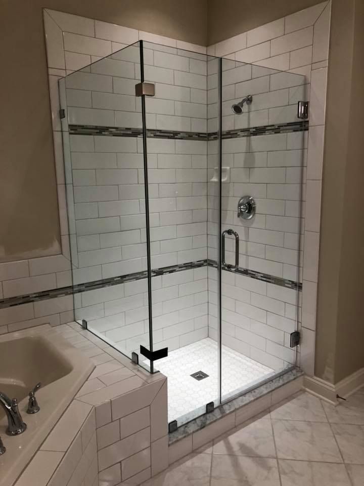 Glass shower enclosure in a bathroom with white tile and decorative trim.