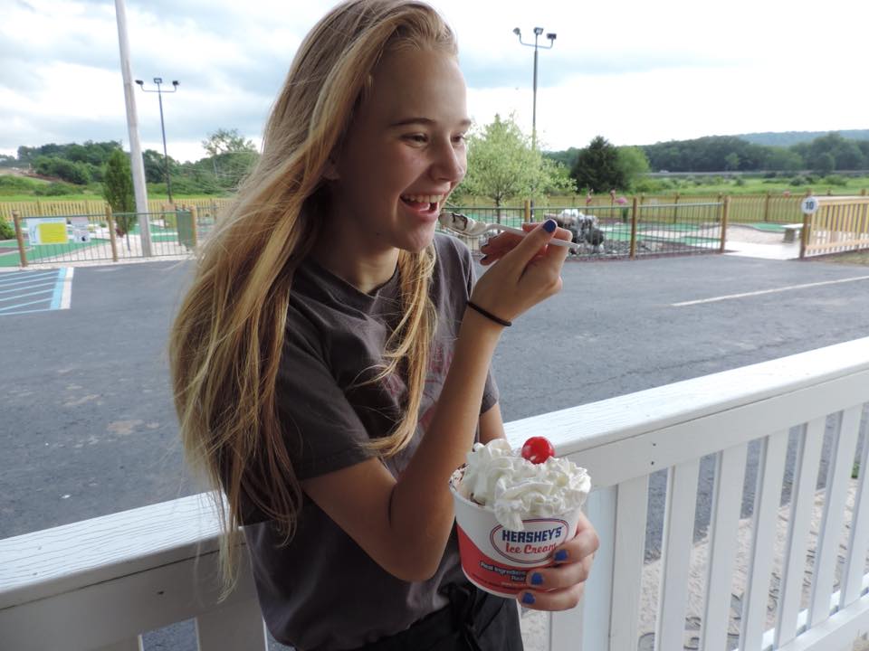 A young girl is eating an ice cream cone with whipped cream and a cherry on top.