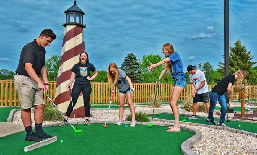 A group of people are playing mini golf in front of a lighthouse.