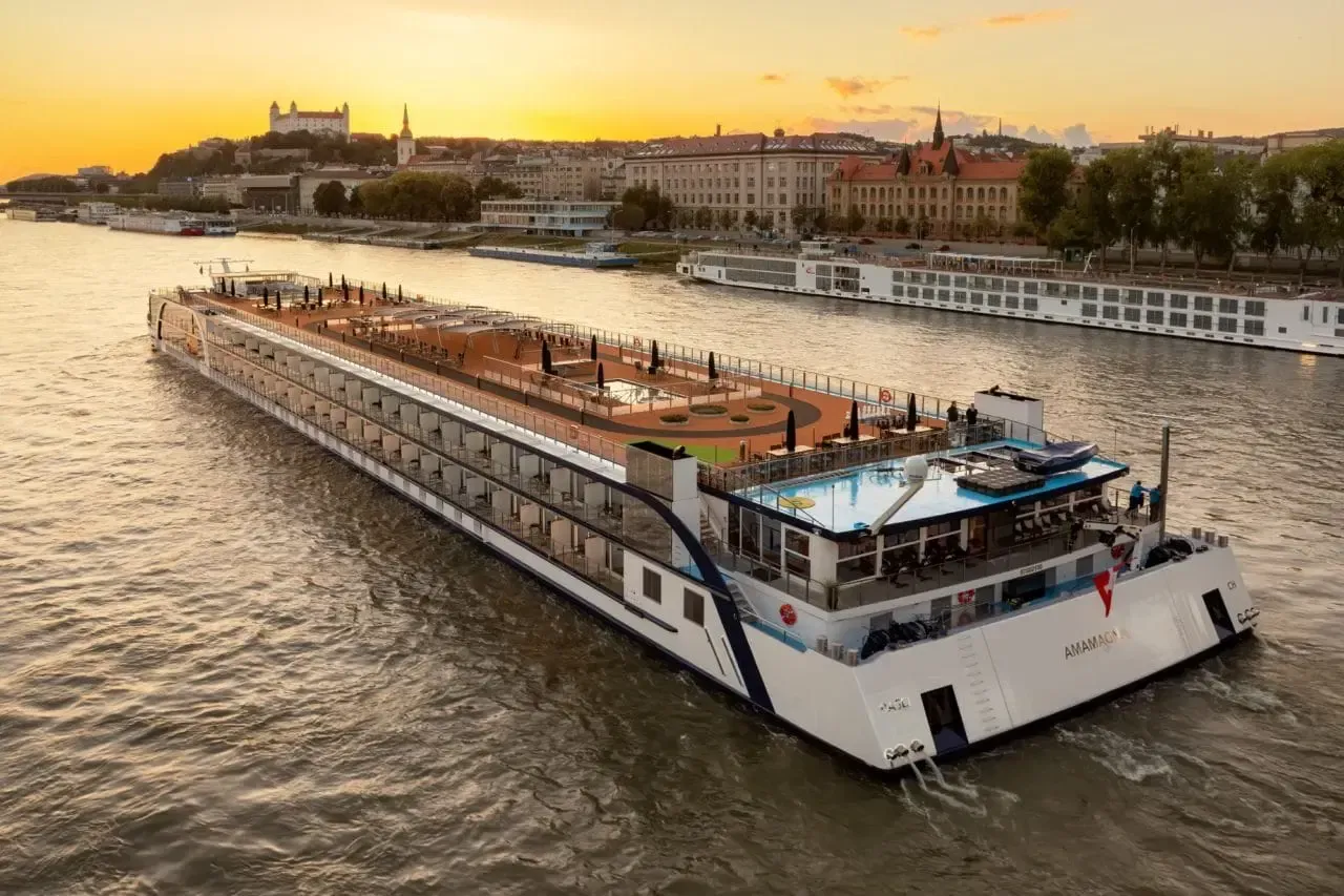 River cruise ship on a sunset-lit river beside a city waterfront