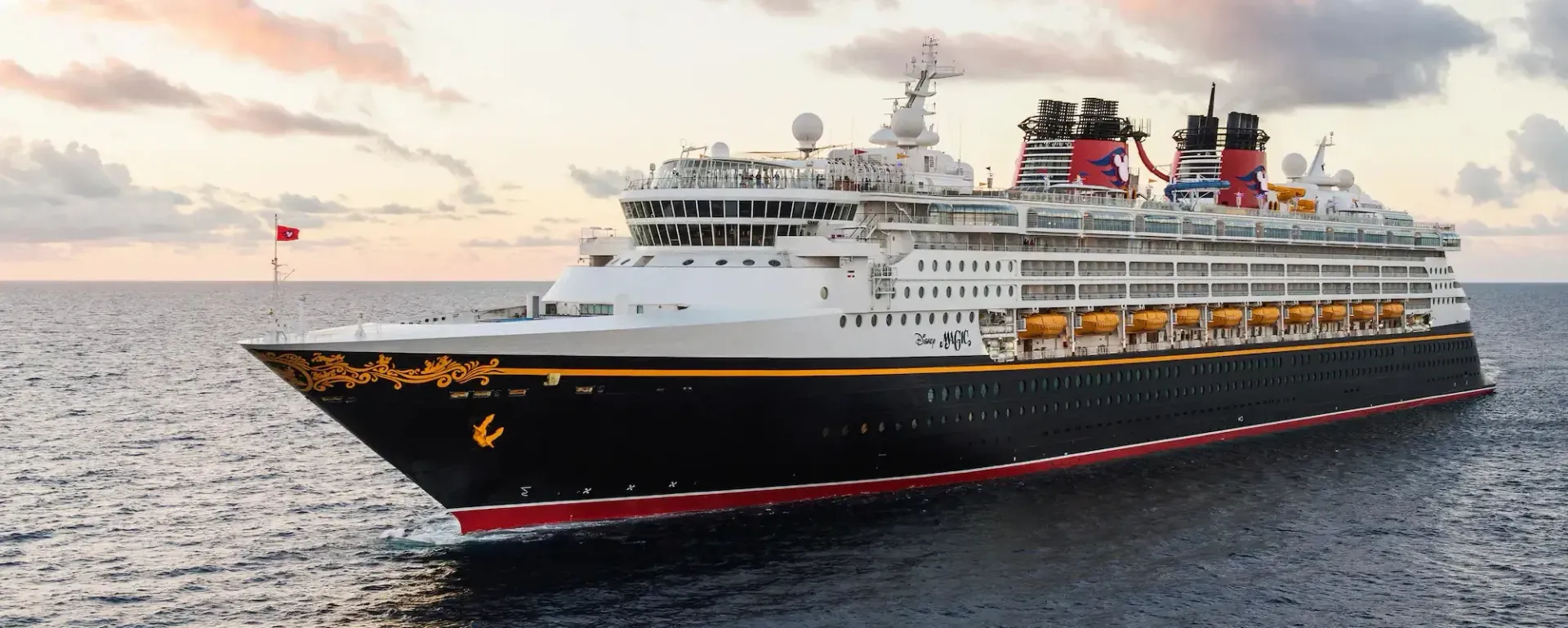 Large black-and-white cruise ship sailing on calm water at sunset with red funnels and warm sky