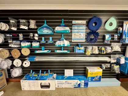 Pool cleaning supplies are displayed on a black slat wall, including brushes, vacuums, and replacement parts. — Tweed Pool Shop in Tweed Heads South, NSW