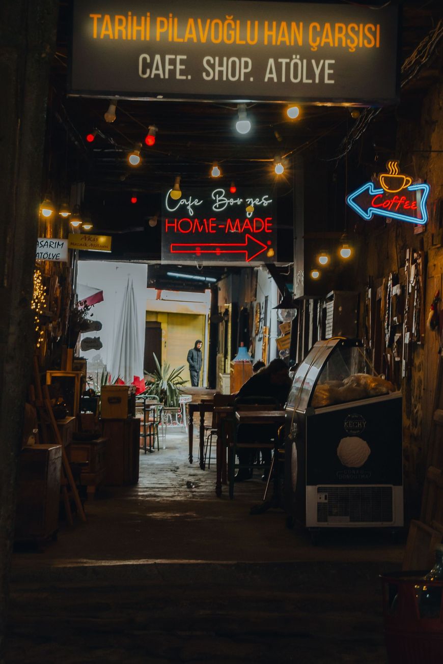 Narrow café and shop entrance at night, lit by warm neon signs and hanging lanterns.