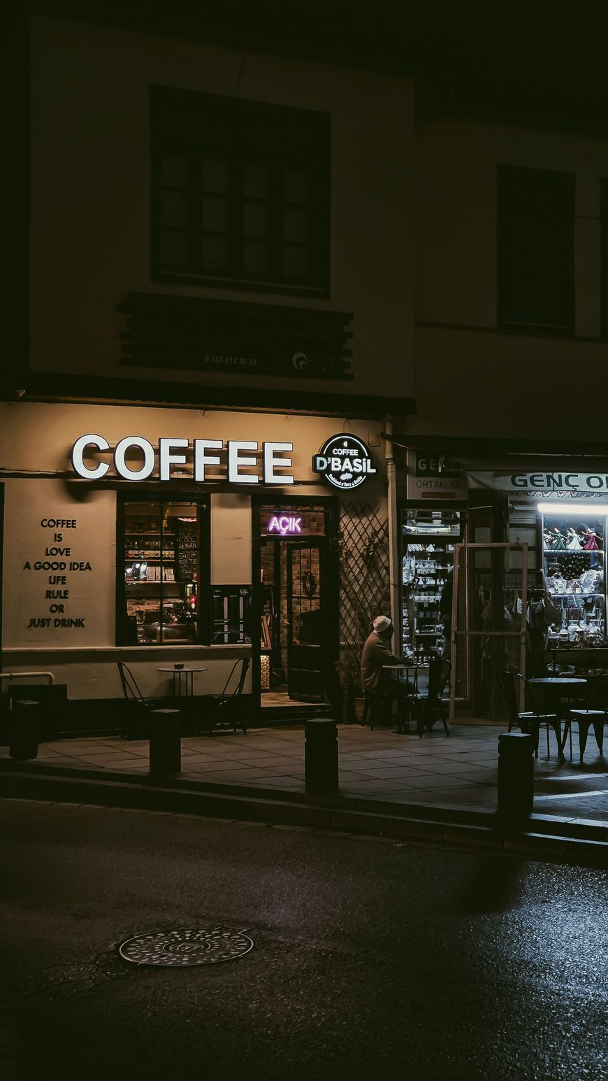 Nighttime coffee shop storefront with glowing sign and wet street reflections