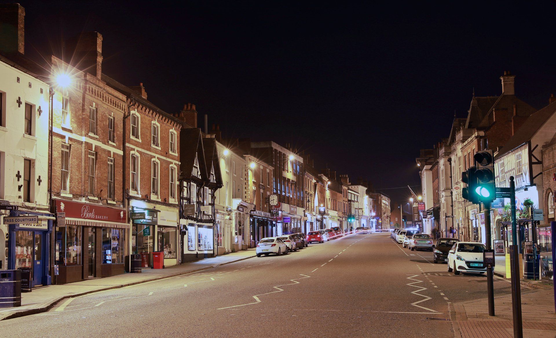 A city street at night with cars parked on the side of the road.