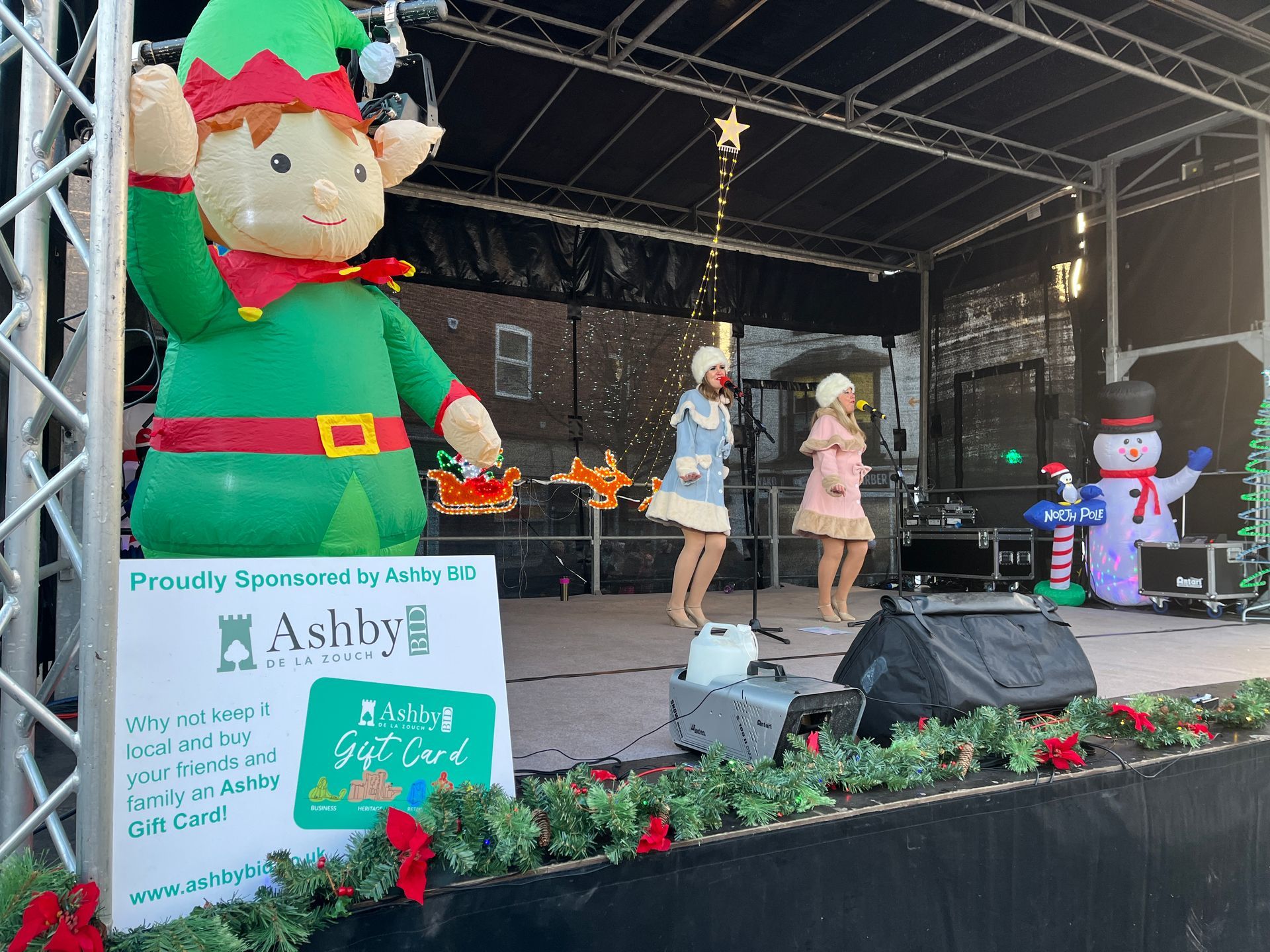 A group of people are standing on a stage in front of a large inflatable elf.