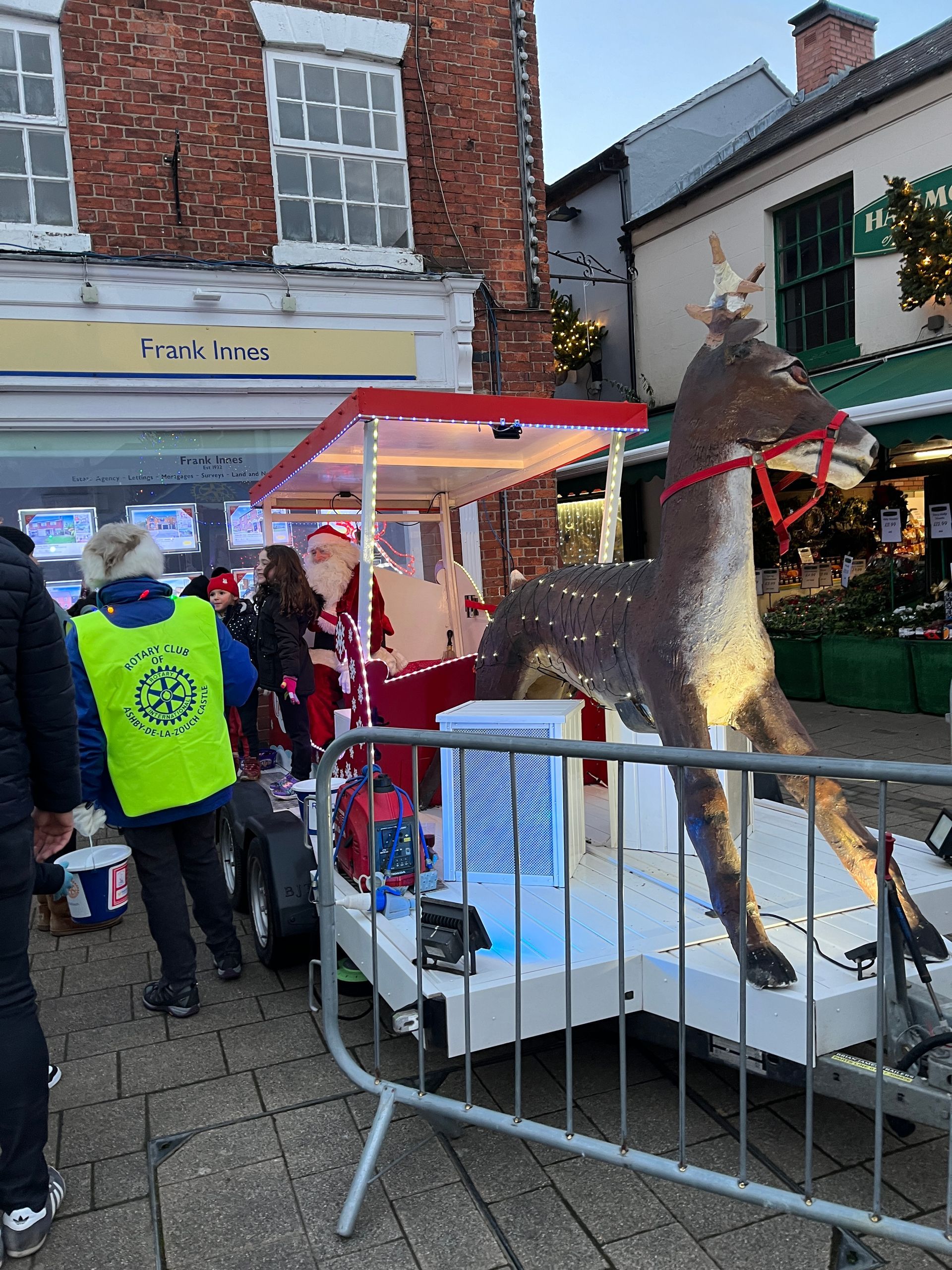 A statue of a reindeer is behind a fence in front of a store.