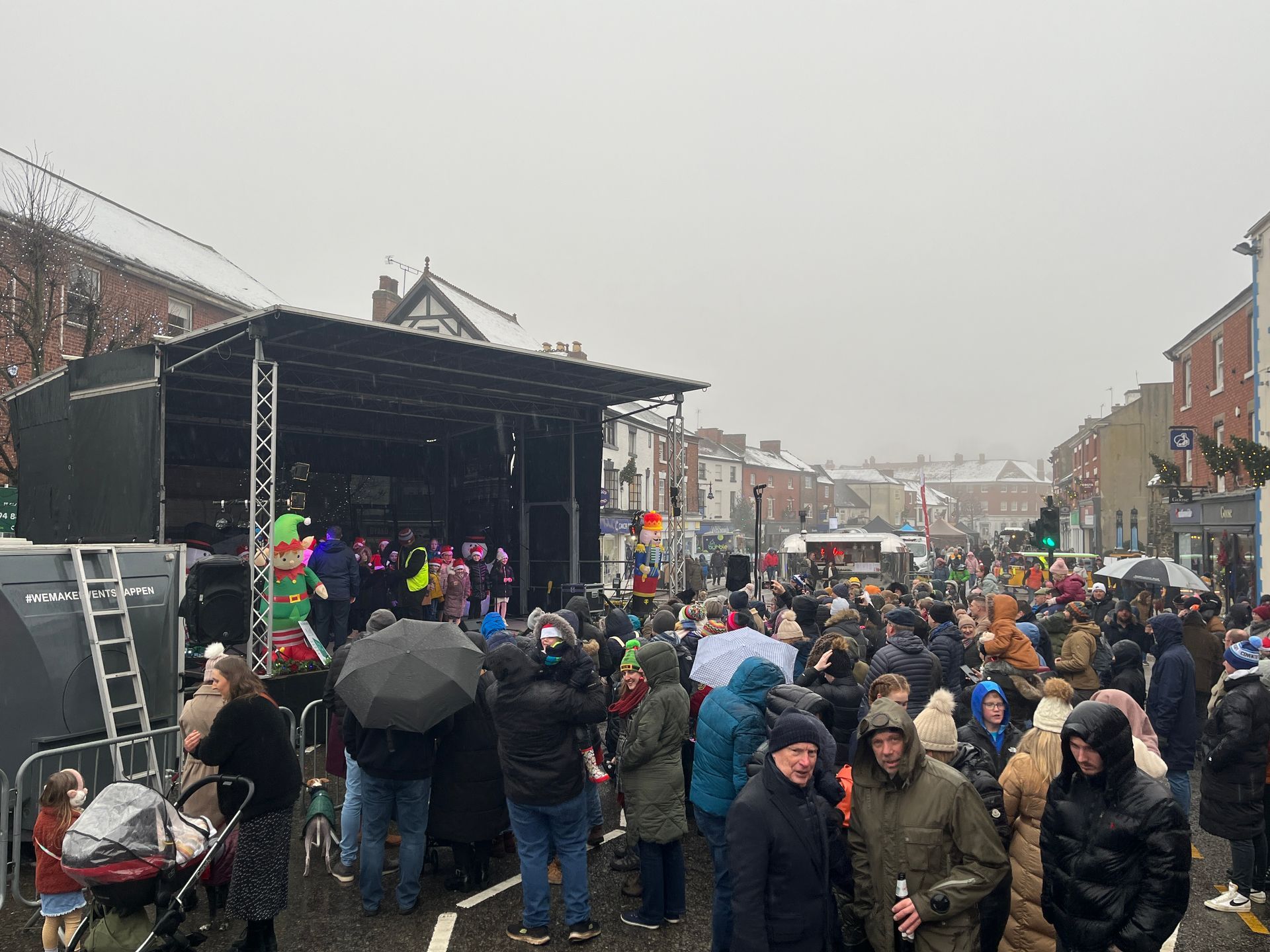 A crowd of people are standing in front of a stage in the rain.