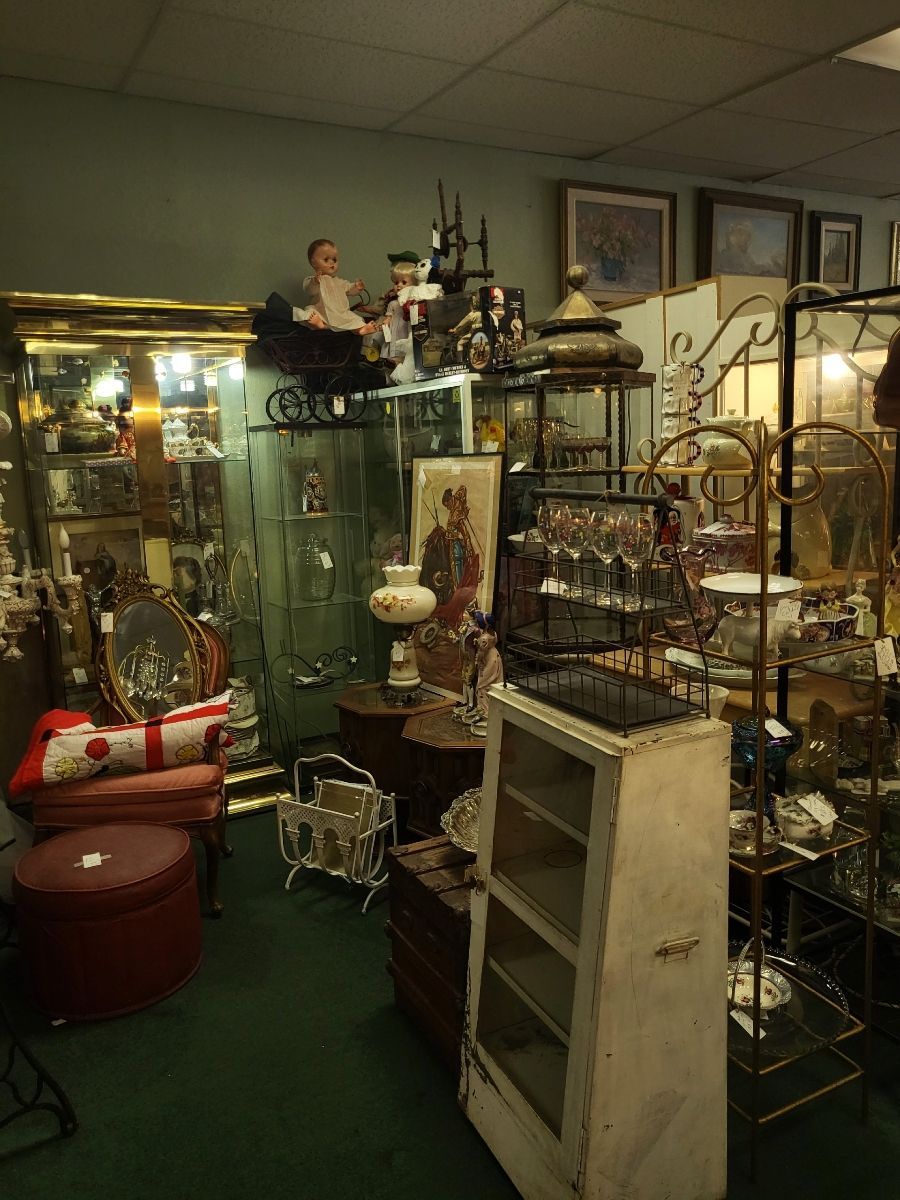 Antique shop interior filled with furniture, decor, and framed artwork. Various items displayed on shelves and tables.