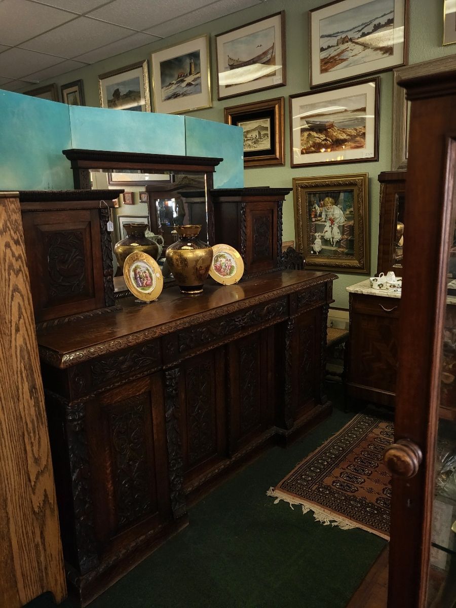 Antique wooden buffet with carvings, mirror, and framed art in a room with green walls and rug.