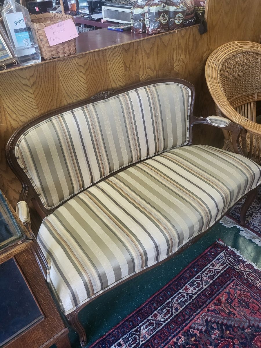 Antique striped loveseat with a wooden frame, on a rug, in a shop.