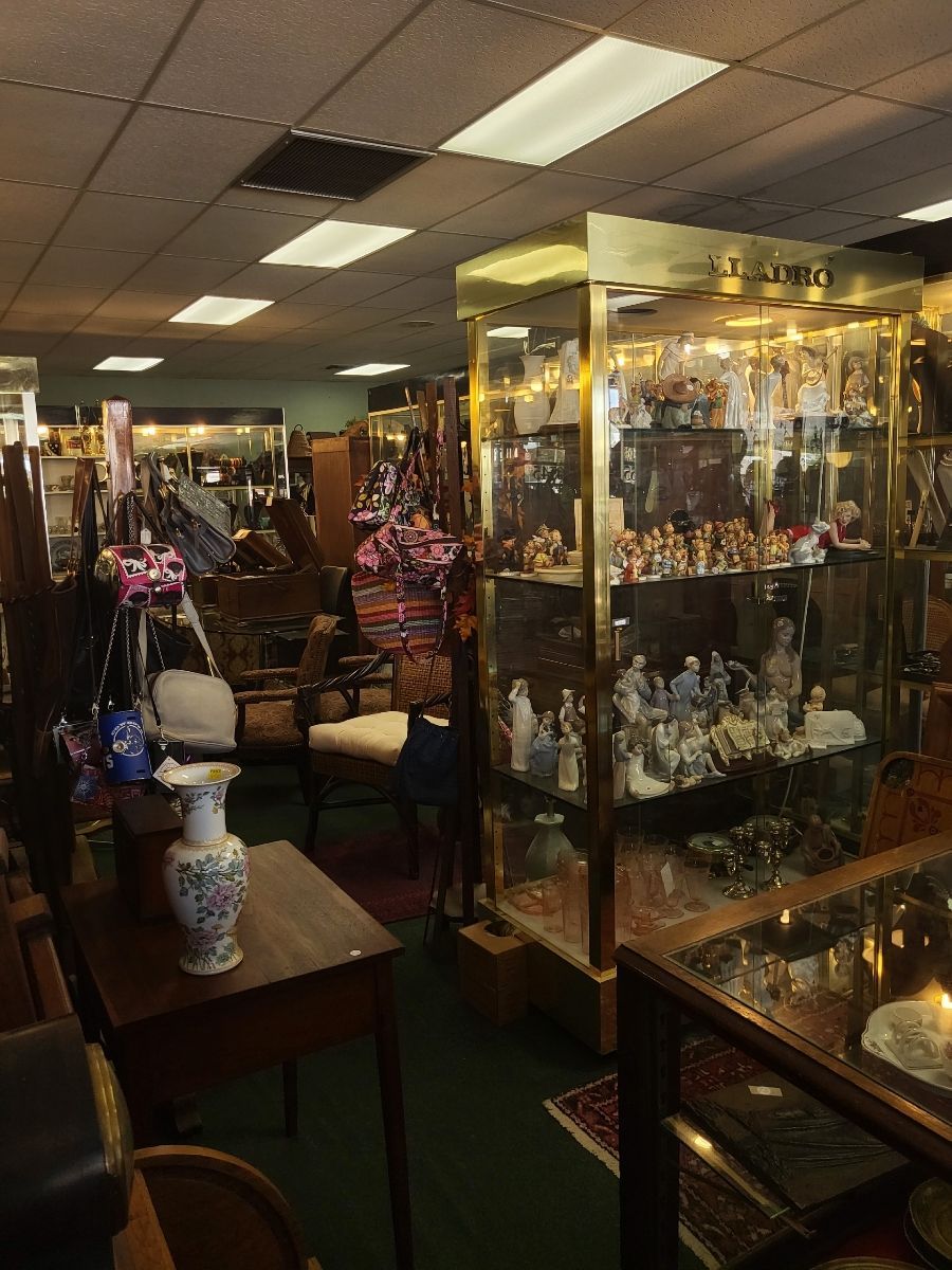 Antique shop interior: display cases of figurines, furniture, lamps, and other items for sale.