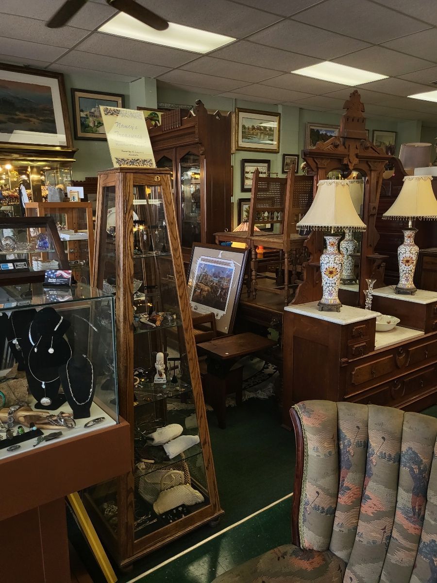 Antique store interior, cluttered with furniture, display cases, and art. Brown wood, muted colors.