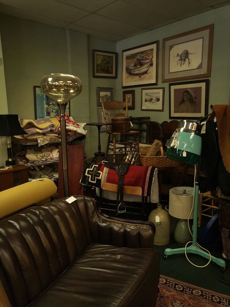 An antique shop interior filled with furniture, art, and lamps against green walls.