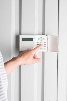 Regolazione manuale di un termostato a parete con tende verticali bianche sullo sfondo.