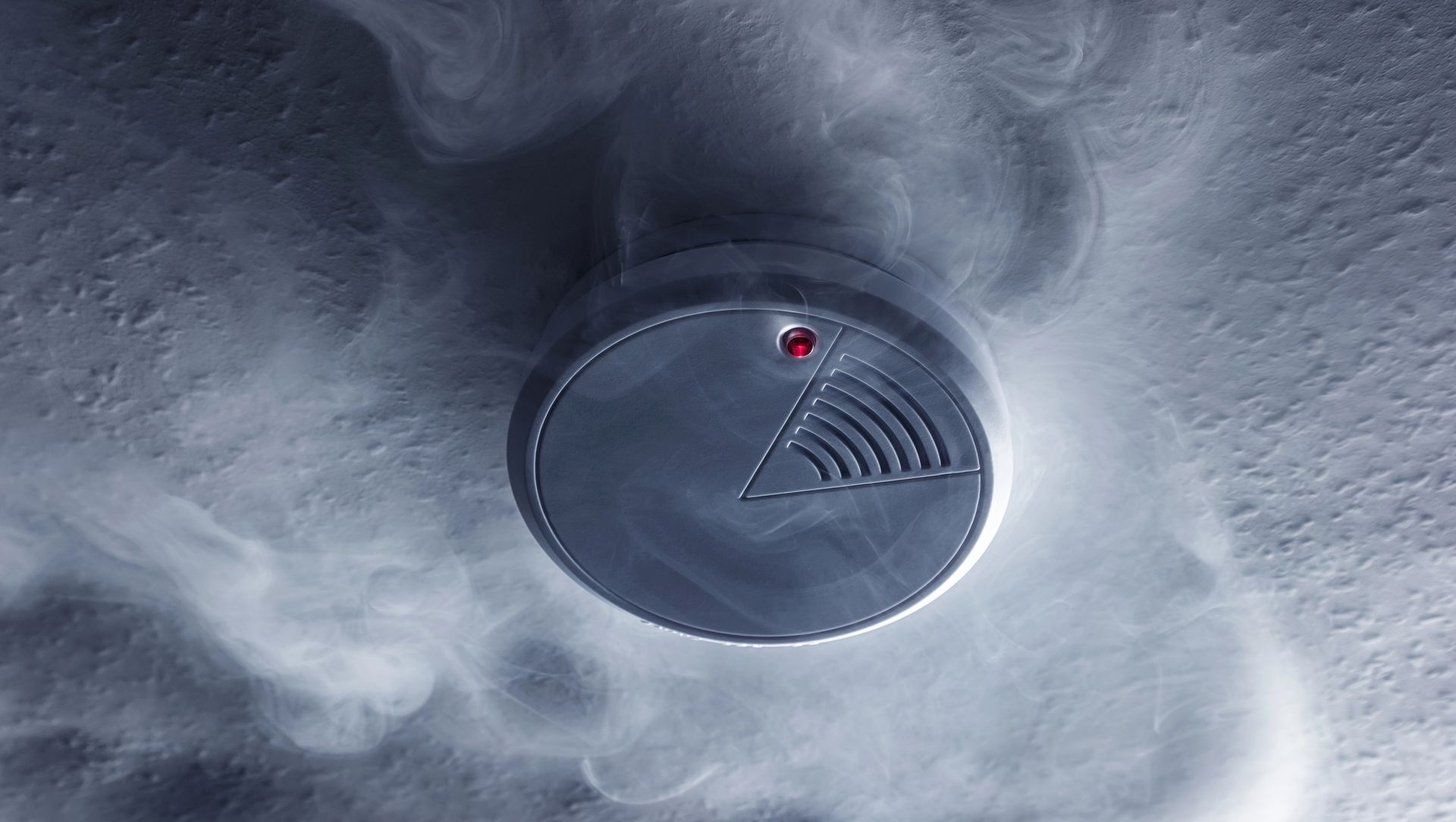 Rivelatore di fumo rotondo con LED rosso sul soffitto, circondato da un vortice di fumo
