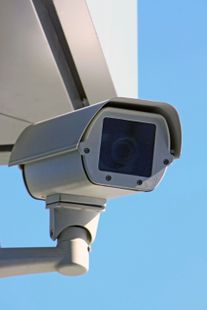 Telecamera di sicurezza installata sotto la sporgenza di un edificio, sullo sfondo di un cielo azzurro.