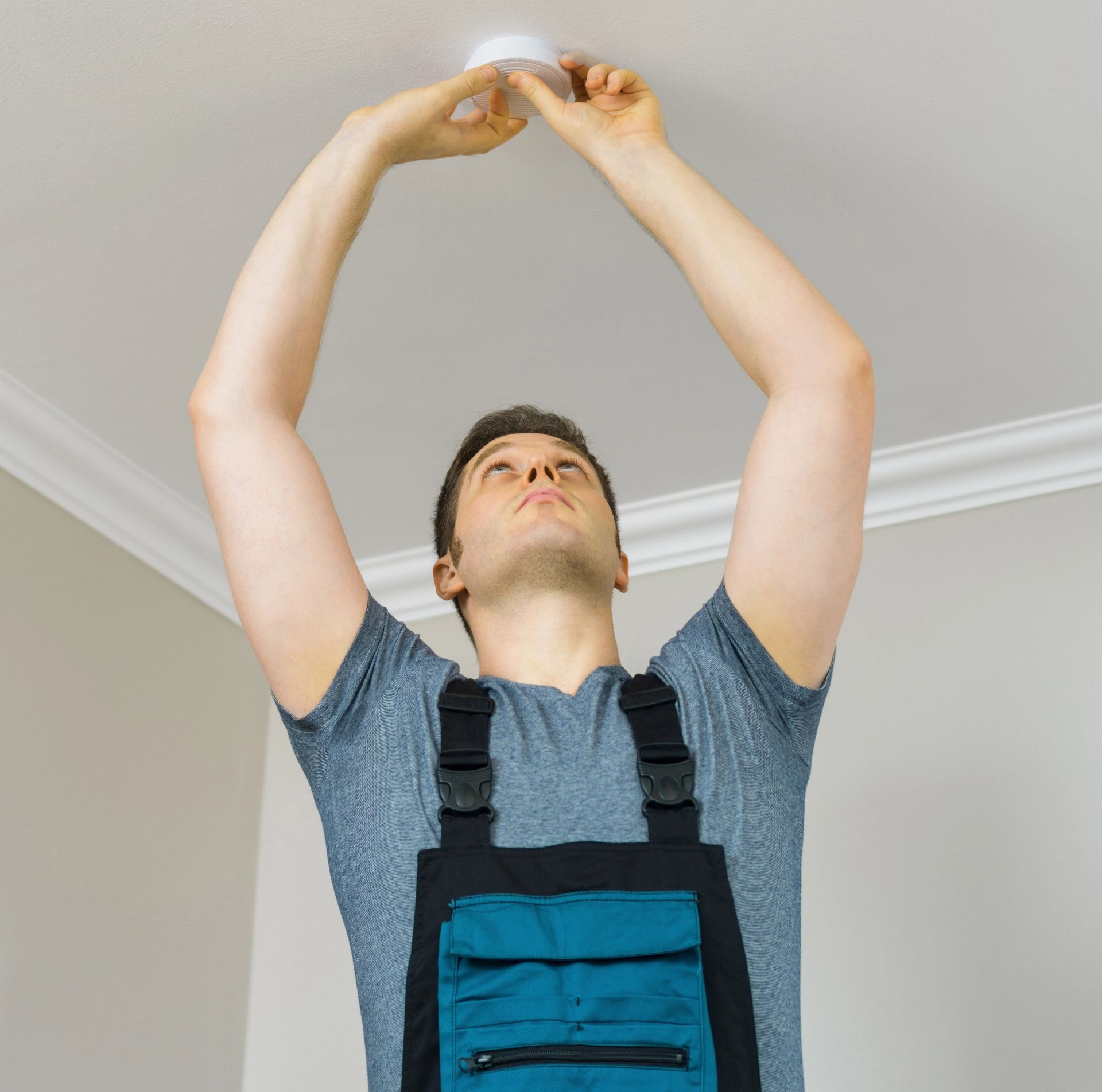 Una persona in tuta blu si allunga per installare un apparecchio di illuminazione a soffitto.