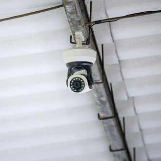Telecamera di sicurezza montata a soffitto, sospesa a una trave metallica in un ambiente interno.