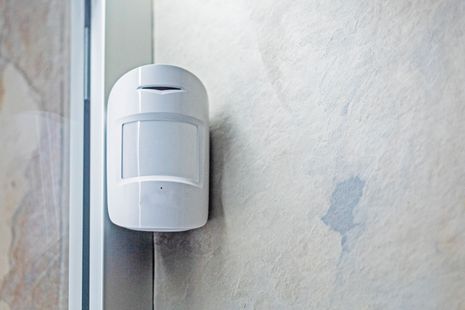Sensore di movimento bianco montato su una parete ruvida vicino a uno stipite della porta.