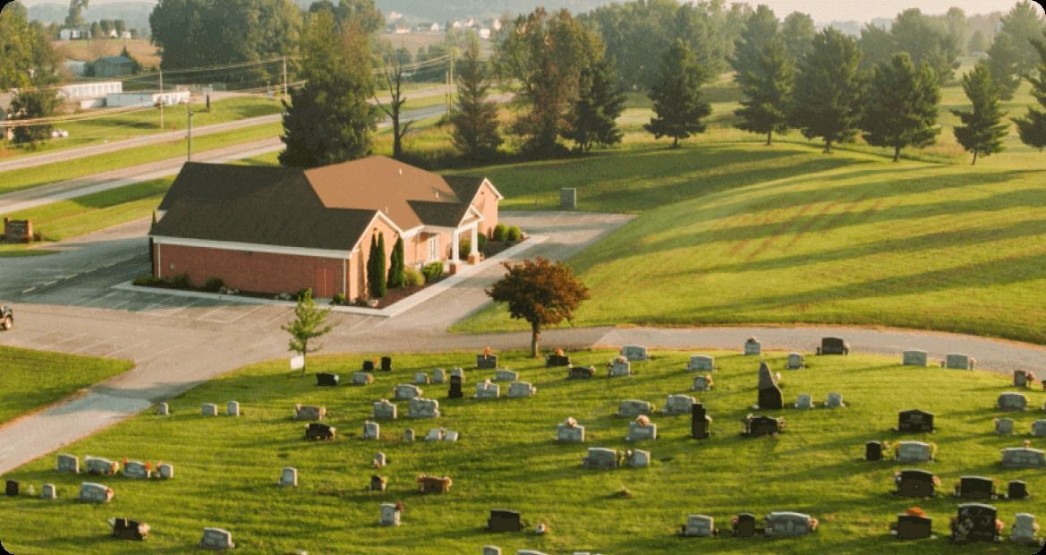 Grassy cemetery with rows of headstones beside a brick chapel on a sunny hillside