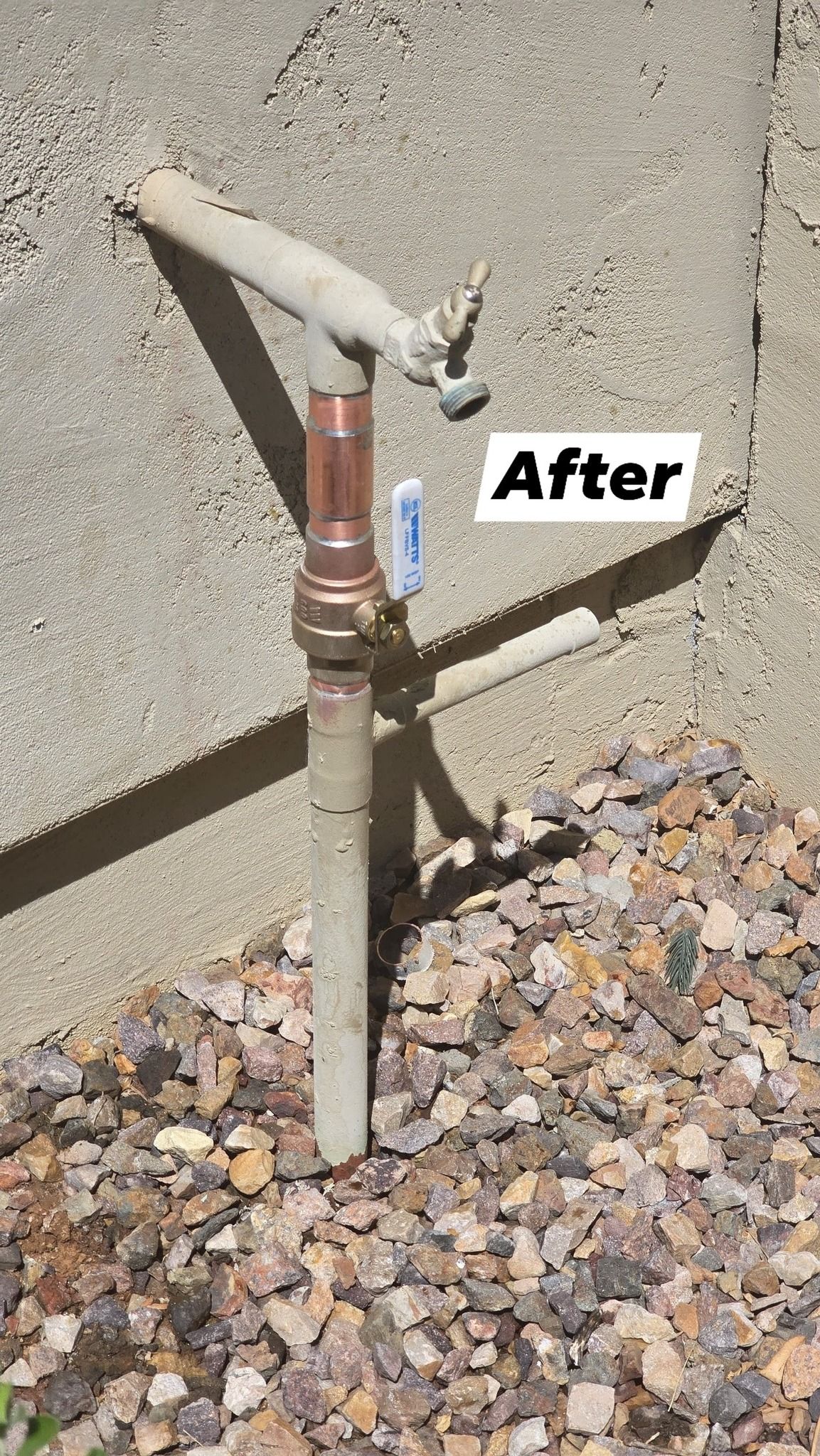 A water faucet is sitting on top of a pile of gravel next to a wall.