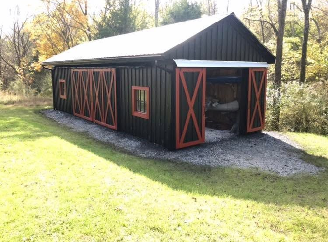 Black barn with red trim and open doors on a grassy lawn, surrounded by trees