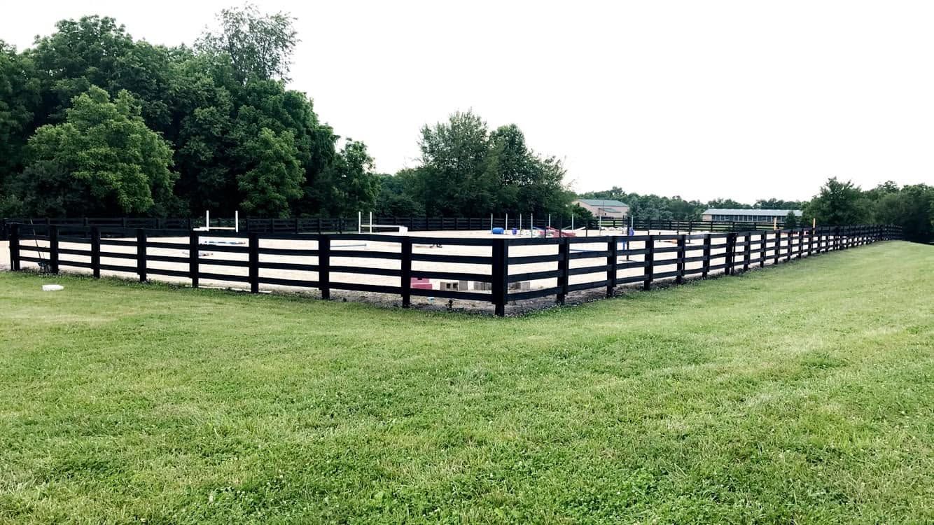 Black fenced horse paddock on a grassy field with trees in the background