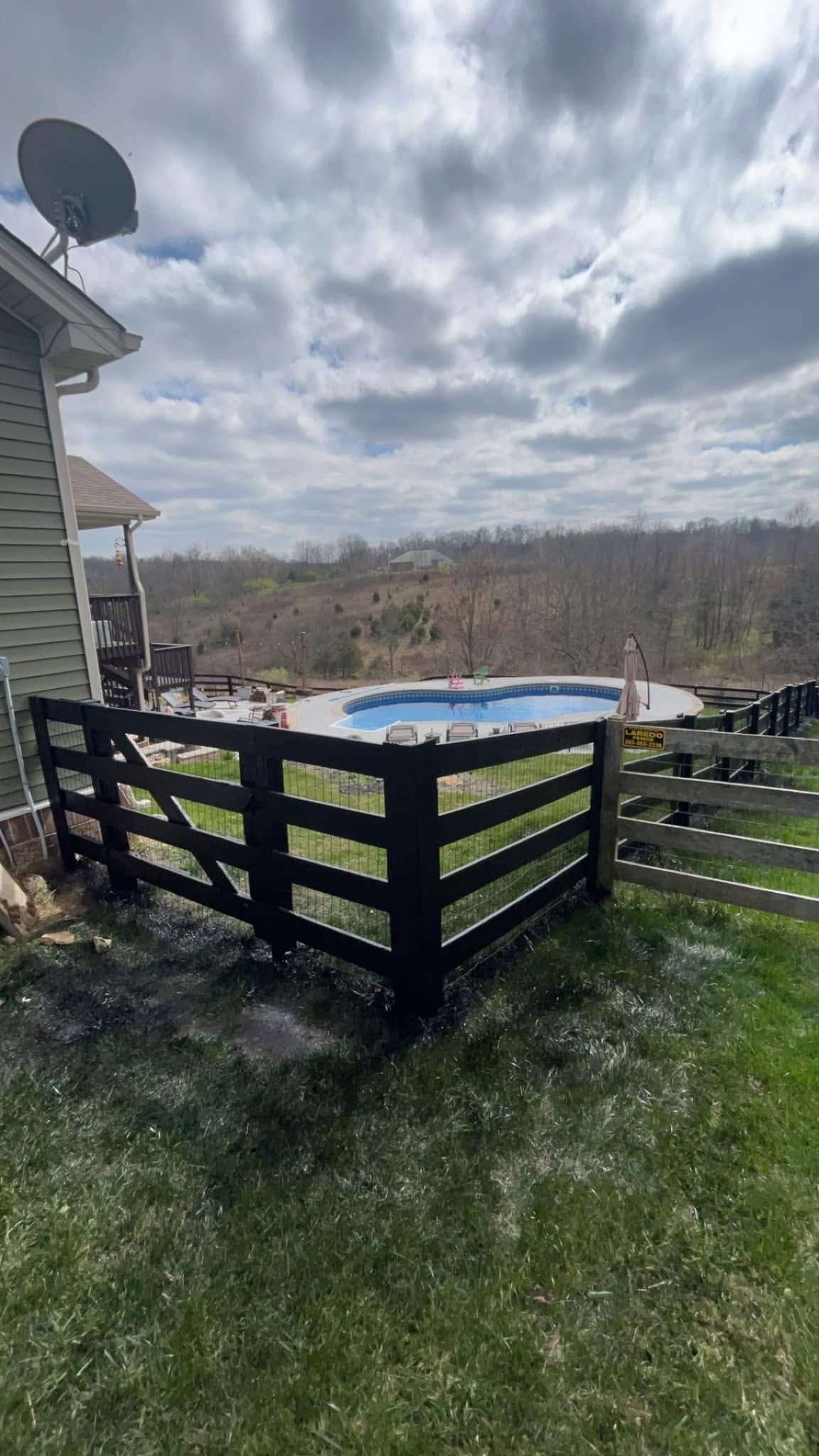 Backyard with above-ground pool surrounded by black fence beside a house under cloudy sky
