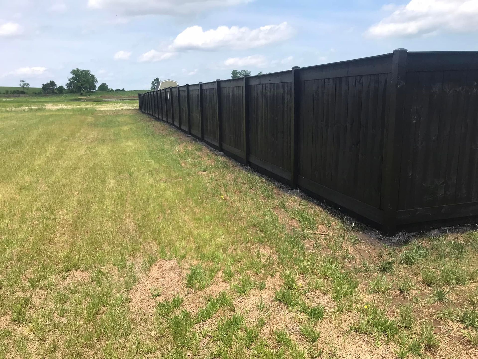 Black fence along a grassy field under a cloudy sky
