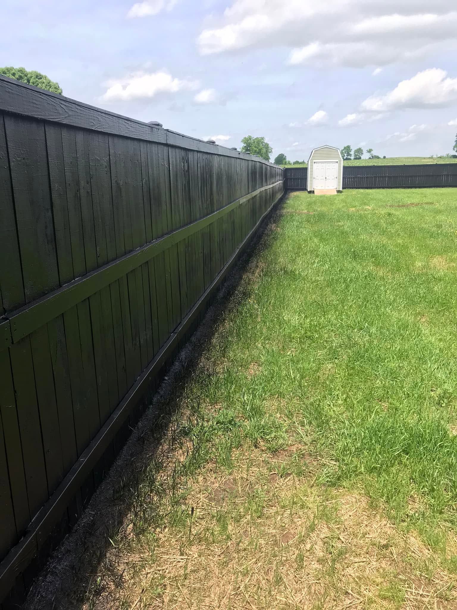 Long black fence beside a grassy yard under a partly cloudy sky
