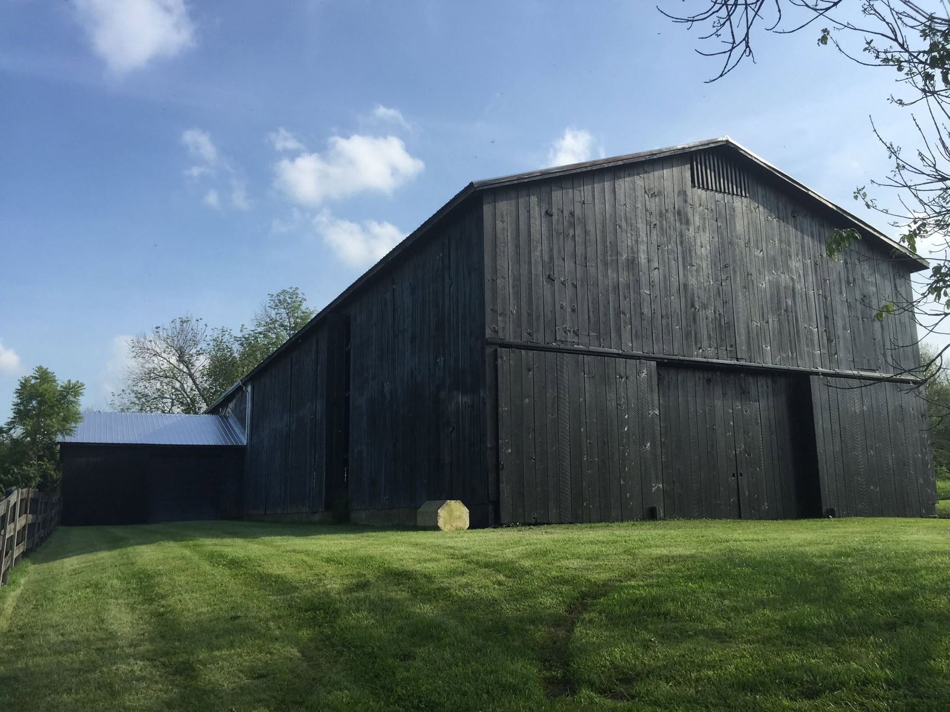 Large black barn on a grassy hill under a blue sky with clouds