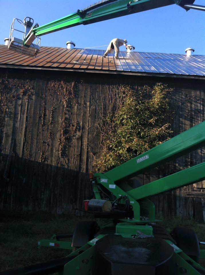Two green boom lifts with workers inspecting a steep, vine-covered roof in bright daylight