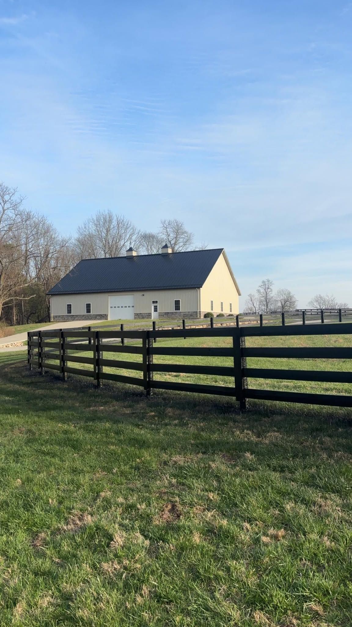Cream-colored barn behind a dark wooden fence in a grassy field under a blue sky