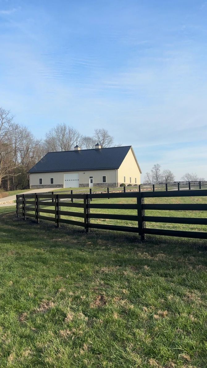 Cream-colored barn behind a dark wooden fence in a grassy field under a blue sky