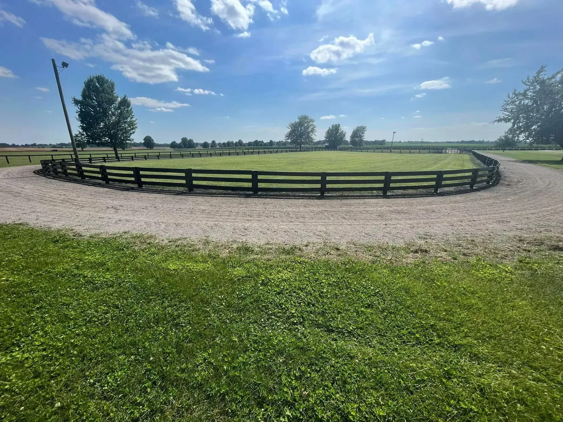 Curved wooden fence around a grassy field under a bright blue sky with clouds