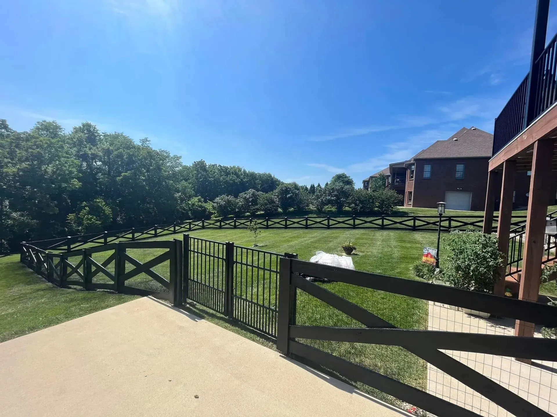 Sunny backyard with a fenced green lawn, pond, and brick house under a blue sky